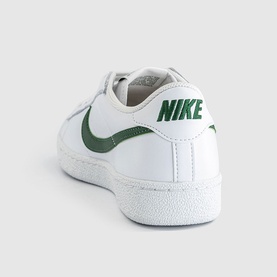 Nike trainer in white with green Swoosh logo and branding, leather upper, white rubber sole, heel view