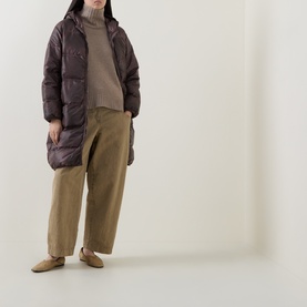 Model wearing Transit rust quilted puffer coat with high collar, styled with beige knit, khaki wide-leg trousers and flat mules.