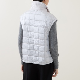 Model wearing Transit gilet in ice white, quilted sleeveless design, styled with grey knit top and black trousers, seen from behind.