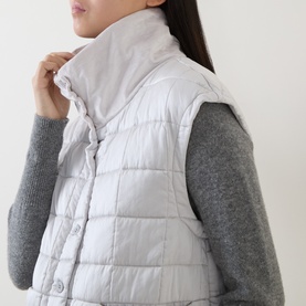 Model wearing Transit gilet in ice, quilted sleeveless design with high collar, styled with grey knit sweater underneath