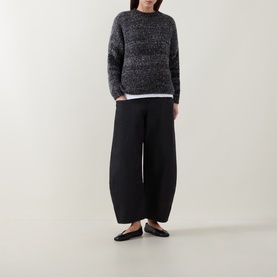 Model wearing dark grey marled knit sweater with white underlayer, black wide-leg trousers, and black flat shoes