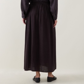 Model wearing Transit skirt in Choco, maxi length with gathered waist, styled with matching top and black flat mules, rear view