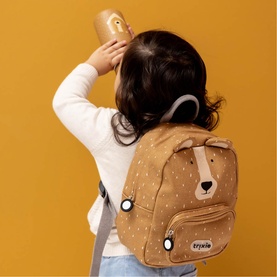 Model carrying Trixie brown bear-print mini backpack with embroidered face detail, worn by a young child facing away
