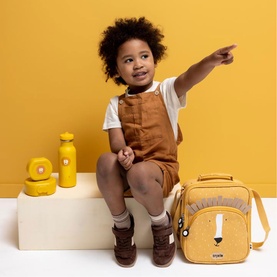 Model carrying Trixie orange lion backpack, styled with matching yellow water bottle and snack pot set on yellow background