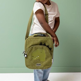 Model carrying Trixie green dinosaur crossbody bag with zip closure, styled on child wearing white tee and jeans