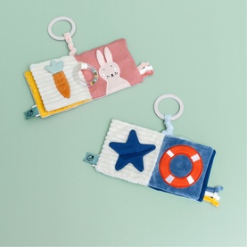 Trixie soft activity books in pink and navy, featuring bunny and star designs with ring clips and sensory textures, shown on green background
