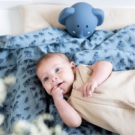 Trixie blue mouse-shaped night light beside a baby lying on a blue elephant-print blanket in a cot