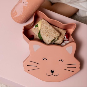 Trixie pink cat-shaped silicone lunch box with smiling face detail, shown open with sandwich inside, matching bottle in background