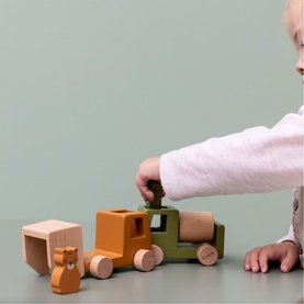 Trixie wooden stacking toy train in olive, orange and natural tones, played with by a young child against a sage green background