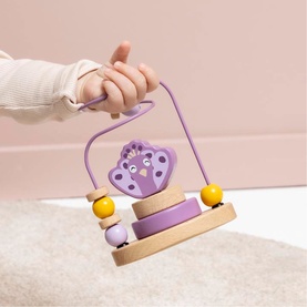 Trixie wooden bead maze toy in purple and natural wood tones with yellow beads, held by a baby's hand