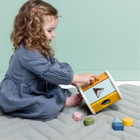Young child playing with Trixie wooden shape-sorter box in multi-colour, with pastel shaped blocks on quilted playmat