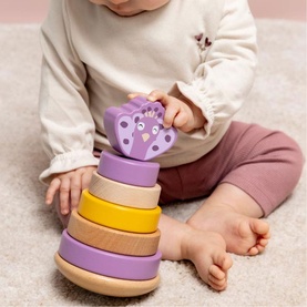 Baby playing with Trixie wooden stacking toy in pastel purple and yellow, topped with a purple animal-shaped piece.