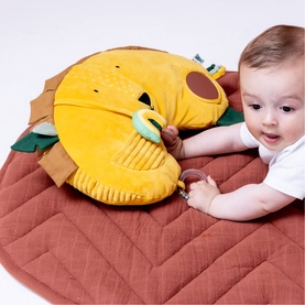 Trixie orange lion play mat with attached plush toy, shown with baby reaching for teething ring on terracotta quilted mat