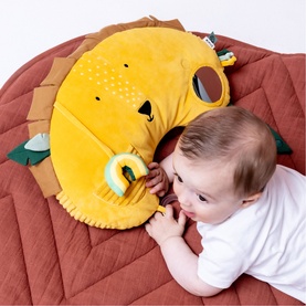 Baby lying on Trixie orange lion activity play mat with mirror and sensory toys, tummy time cushion visible