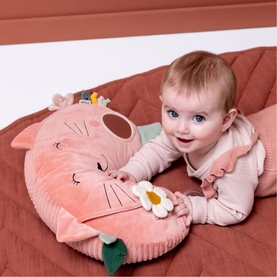 Trixie pink cat-shaped baby activity cushion with daisy detail, shown with smiling baby lying on top on a rust quilted surface