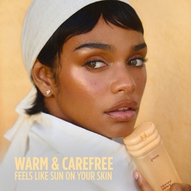Model with Gisou Body Mist held close to face, glowing skin, wearing white head wrap, warm golden-toned campaign shot