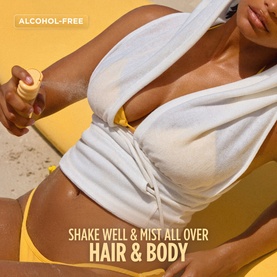 Gisou Hair & Body Mist being sprayed, alcohol-free formula, shown in a beach lifestyle setting with text overlay.