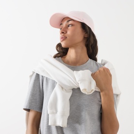 Model with Lululemon Classic Ball Cap in Pink Pearl, paired with grey T-shirt and white sweatshirt draped over shoulders