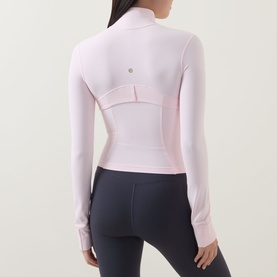 Model wearing Lululemon Pink Pearl jacket, back view, with thumbhole cuffs and seam detailing, styled with dark grey leggings