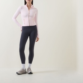Model wearing Lululemon Pink Pearl zip-up fitted jacket with navy leggings, white socks and grey trainers.