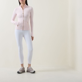 Model wearing Lululemon Pink Pearl zip-up jacket with gold zip detail, styled with white leggings and grey trainers.