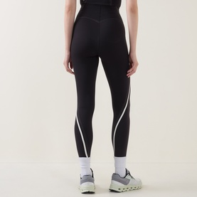 Model wearing Lululemon black leggings with light ivory contrast seam detailing, rear view, styled with grey and white trainers.