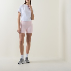Model wearing Lululemon Pink Pearl bike shorts, styled with a white crop tee and grey trainers.