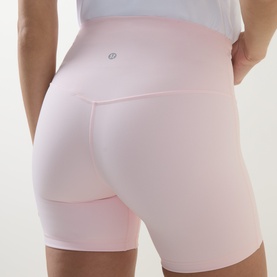 Model wearing Lululemon Pink Pearl high-waist cycling shorts, rear view, with a white cropped top.