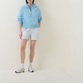 Model wearing Lululemon Heathered Core Ultra Light Grey shorts, styled with a light blue half-zip sweatshirt and grey trainers.