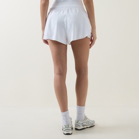 Model wearing Lululemon white shorts, shown from behind, styled with white crop top, white socks and grey trainers.