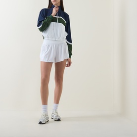 Model wearing Lululemon white shorts with navy and green colour-block windbreaker, white socks and grey trainers.