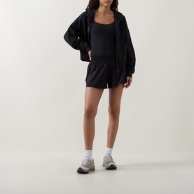 Model wearing Lululemon black shorts with matching black bodysuit and oversized zip-up hoodie, styled with white socks and grey trainers.