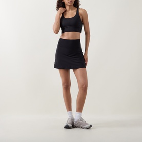 Model wearing Lululemon black skirt with matching sports bra crop top and white ankle socks with grey trainers.