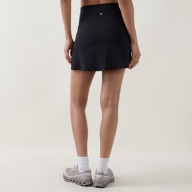 Model wearing Lululemon black skirt, rear view, styled with white socks and grey trainers.