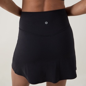 Model wearing Lululemon black high-waisted sports skirt with wide waistband and logo badge, rear view.