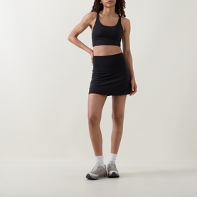 Model wearing Lululemon black mini skirt with matching black sports bra crop top and white ankle socks with grey trainers.