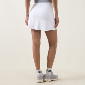 Model wearing Lululemon white tennis skirt, rear view, styled with white ankle socks and grey trainers.