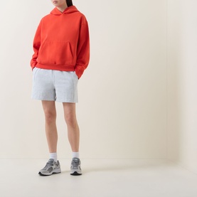 Model wearing Lululemon Cherry Ember oversized hoodie with light grey shorts and white socks with grey trainers.