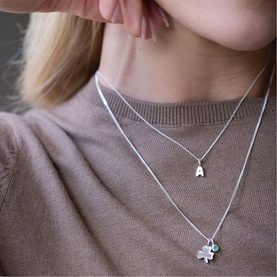 Model with Juvi silver layered necklaces; one featuring a letter A initial pendant, one with a four-leaf clover charm