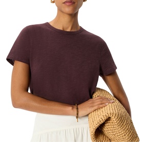 Model wearing Whistles red short-sleeve crew neck T-shirt, styled with a white midi skirt and carrying a woven straw bag.