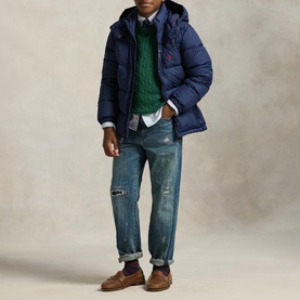 Model wearing Ralph Lauren Newport Navy hooded puffer jacket, styled with green knit, blue shirt, distressed jeans and brown suede shoes.