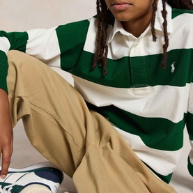 Model wearing Ralph Lauren Iconic Pony Logo Striped Rugby Shirt in cream and green stripes, styled with beige wide-leg trousers.