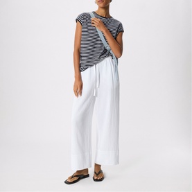 Model wearing Whistles blue and white stripe cap sleeve t-shirt with wide-leg white trousers and black flat sandals.