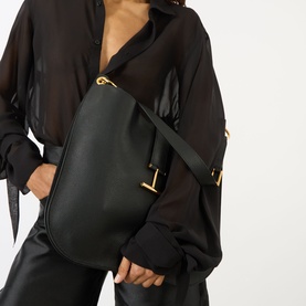 Model carrying Tom Ford Tara Large Crossbody Bag in black calfskin with gold-tone hardware and signature T detail, styled with black sheer shirt