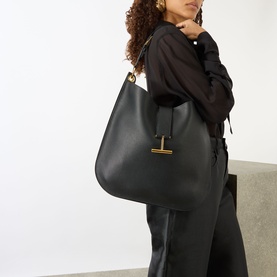 Model carrying Tom Ford Tara Large Crossbody Bag in black calfskin with gold-tone hardware and signature T detail, styled with black outfit