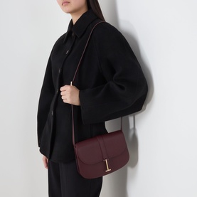 Model carrying Tom Ford Kara Small Crossbody Bag in Lost Cherry grained leather with gold-tone T hardware, worn crossbody over black outfit