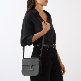 Model carrying Tom Ford Tara Mini Crossbody Bag in black grained calfskin with gold-tone T-bar detail and adjustable strap, styled with all-black