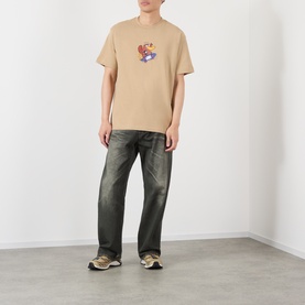Model wearing Vans beige cotton T-shirt with graphic chest print, styled with dark wash wide-leg jeans and trainers.