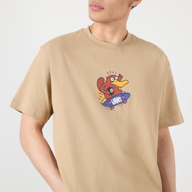 Model wearing Vans beige cotton T-shirt with small chest graphic of cartoon bird on a skateboard with Vans logo.