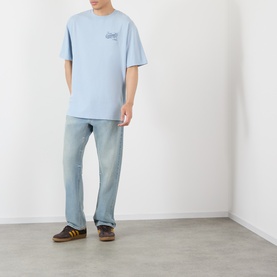 Model wearing Vans light blue oversized cotton T-shirt with small chest graphic, styled with light wash jeans and brown trainers.